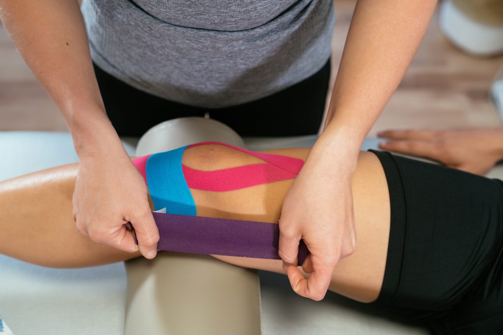 Physiotherapist putting kinesiology tape on patient's knee for prevention of knee pain.