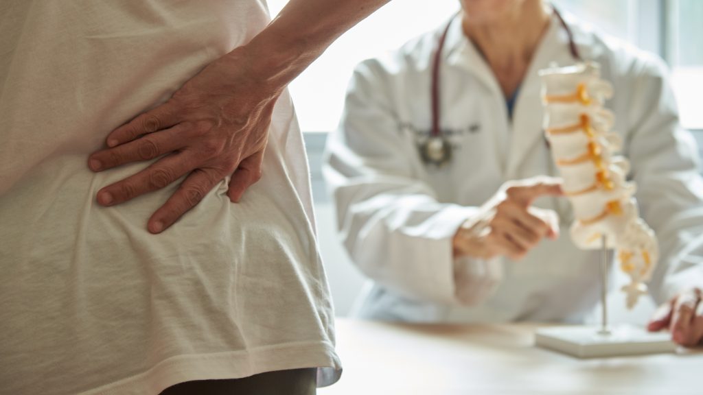 Image shows doctor diagnosing back pain.