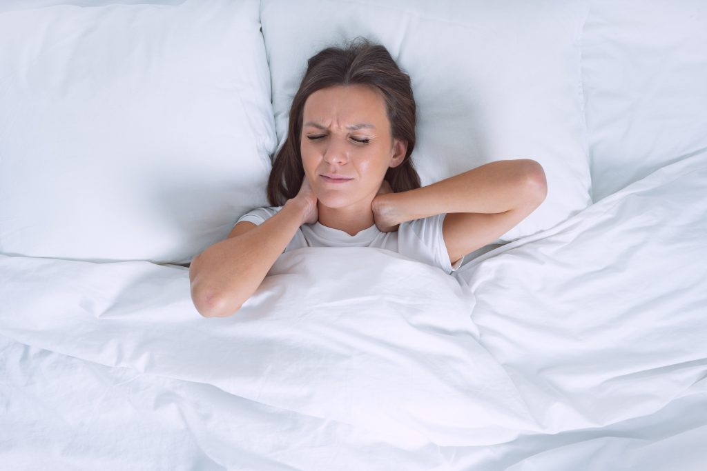 Woman in bed suffering from neck pain after sleeping in uncomfortable pillow.