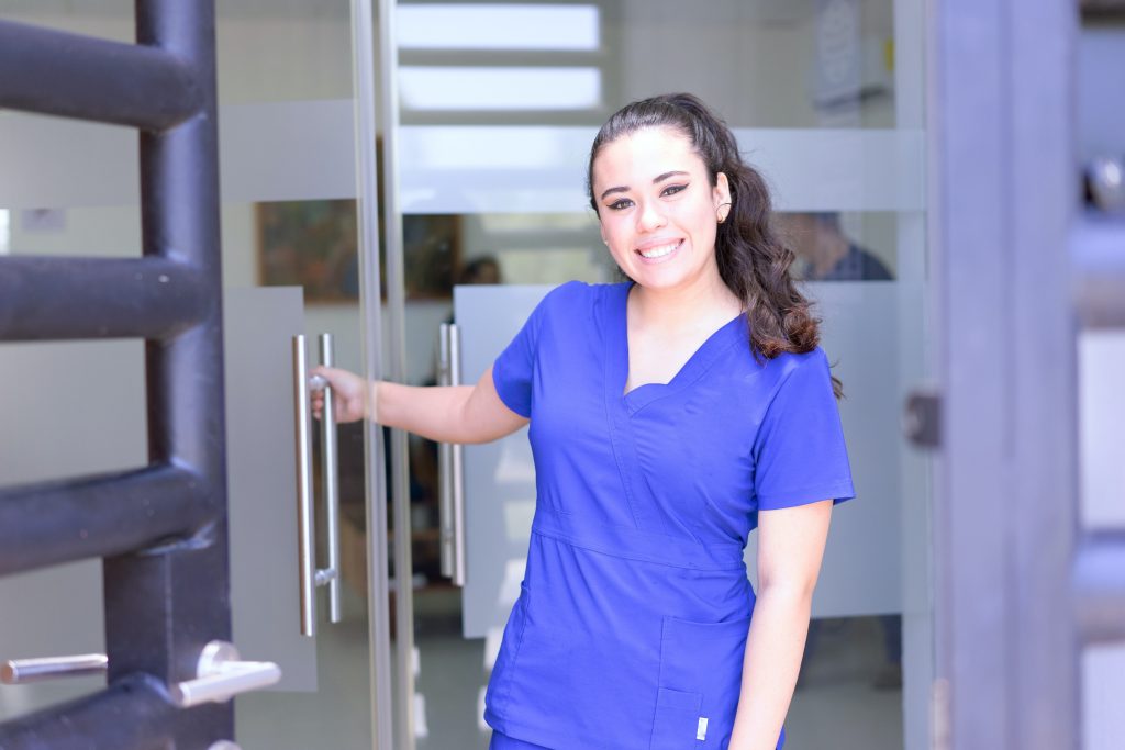 image shows a woman wearing blue scrub suits who is smiling, possibly a physical therapist