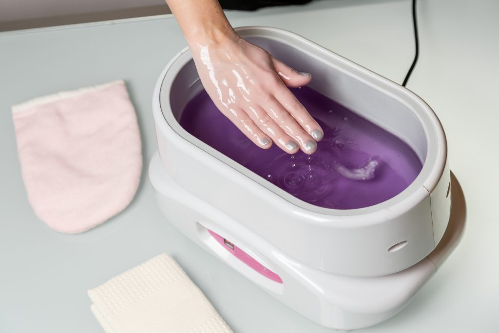 Female hand immersed in paraffin wax bath therapy.
