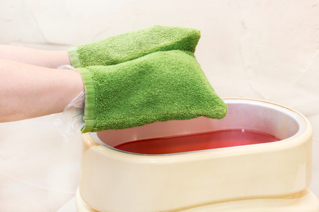 Hands covered in insulated mittens after dipping in paraffin wax bath therapy.