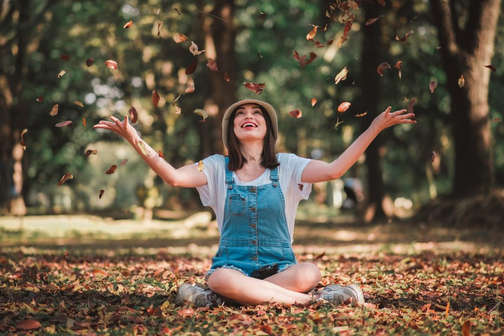 Happy girl sitting on the ground playing with leaves.