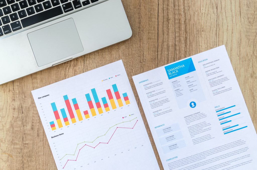A laptop and papers with line graphs and statistics on a table