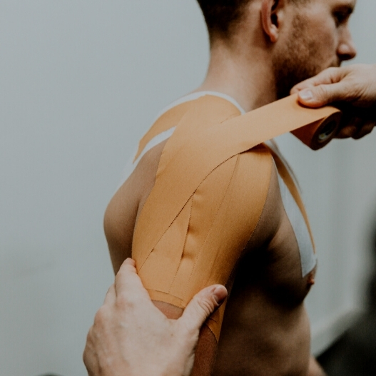A person getting a proper strapping technique for their shoulder while another person adds more tape