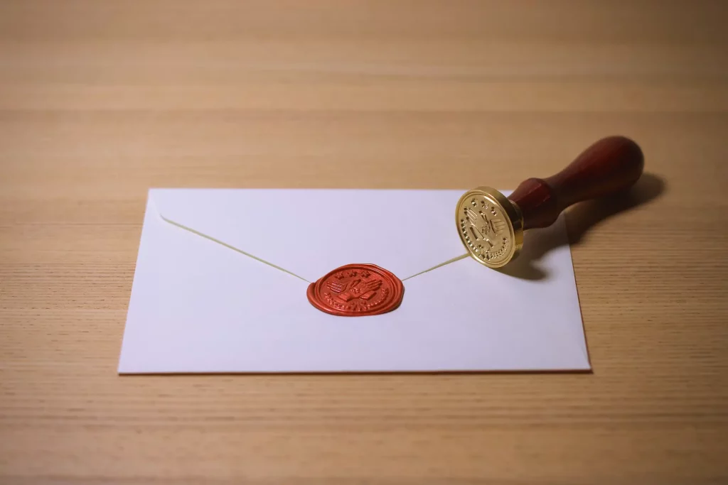 A red wax seal is stamped on a white envelope while the stamp is on its side on the table