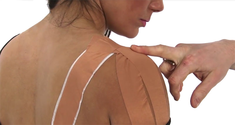 A person is showing their Acromioclavicular Joint Sprain Taping for their AC joint, with a hand pointing to their work with their middle finger