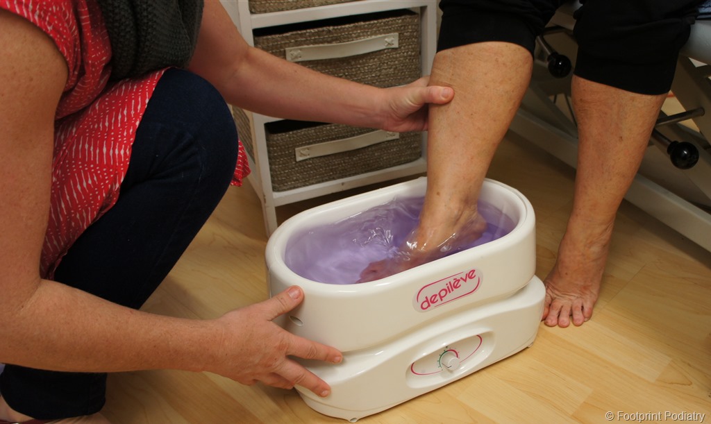 A person is dipping another person's foot in a melted paraffin wax bath