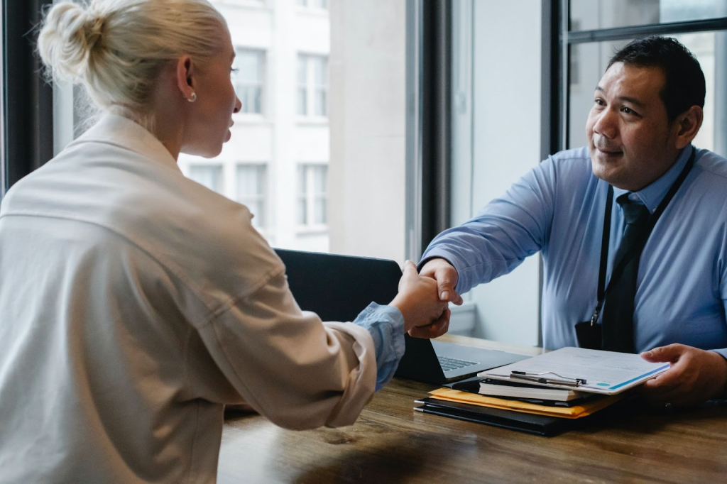 Insurance agent with a ohysiotherapist, talking and shaking hands while sitting down by a desk