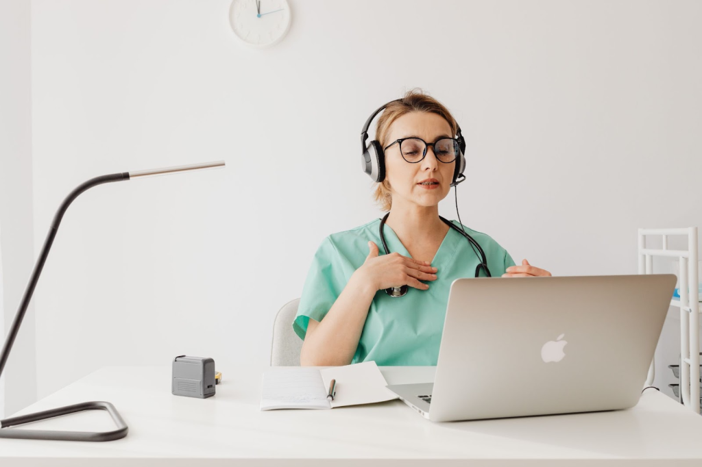 Physiotherapist with headphones on video call with a client, demonstrating an exercise