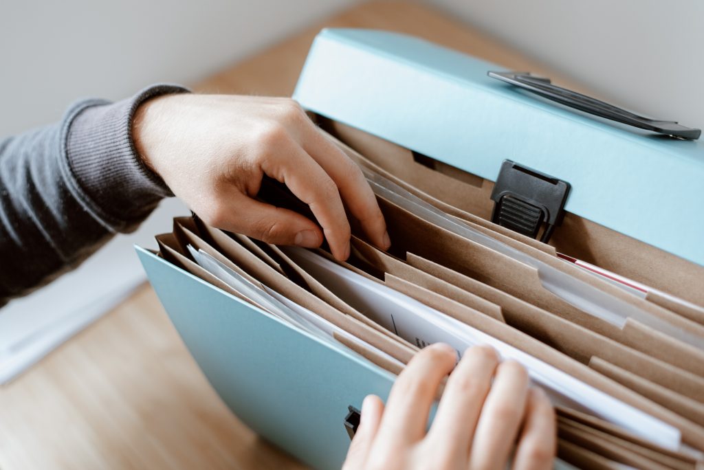 a pair of hands leafing through a bluish-green file case