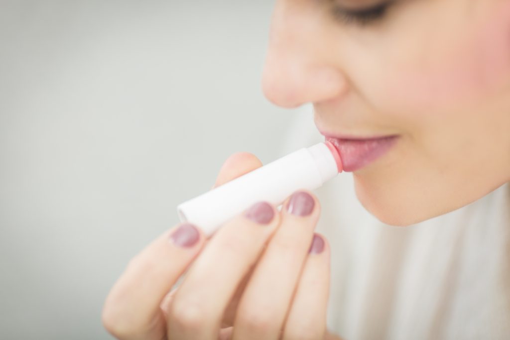 A lady is putting paraffin wax lip balm on their dry lips