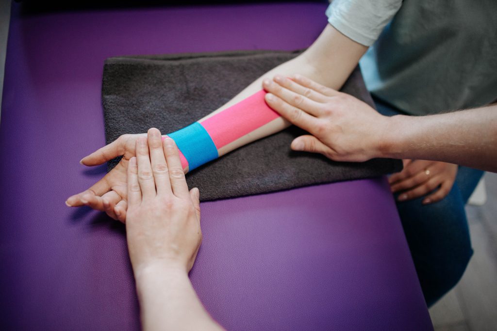 physiotherapist putting athletic tape on a patient's arm on a violet table