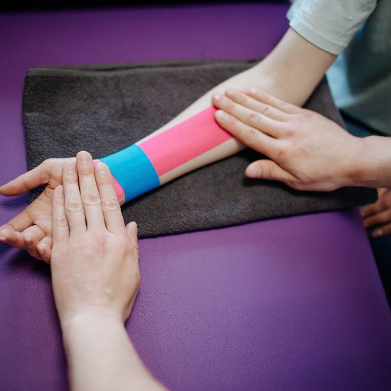 physiotherapist putting athletic tape on a patient's arm on a violet table