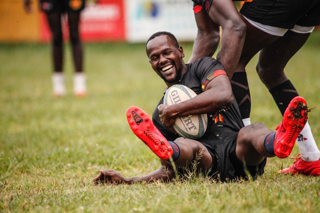 Rugby player smiling and holding the rugby ball while trying to stand up on the field