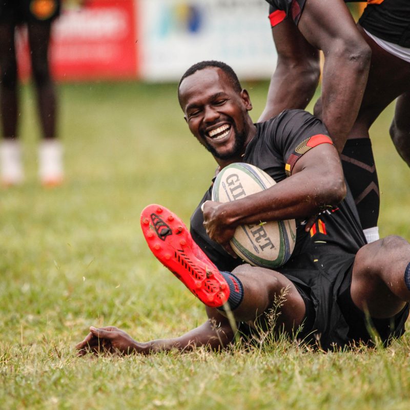 Rugby player smiling and holding the rugby ball while trying to stand up on the field