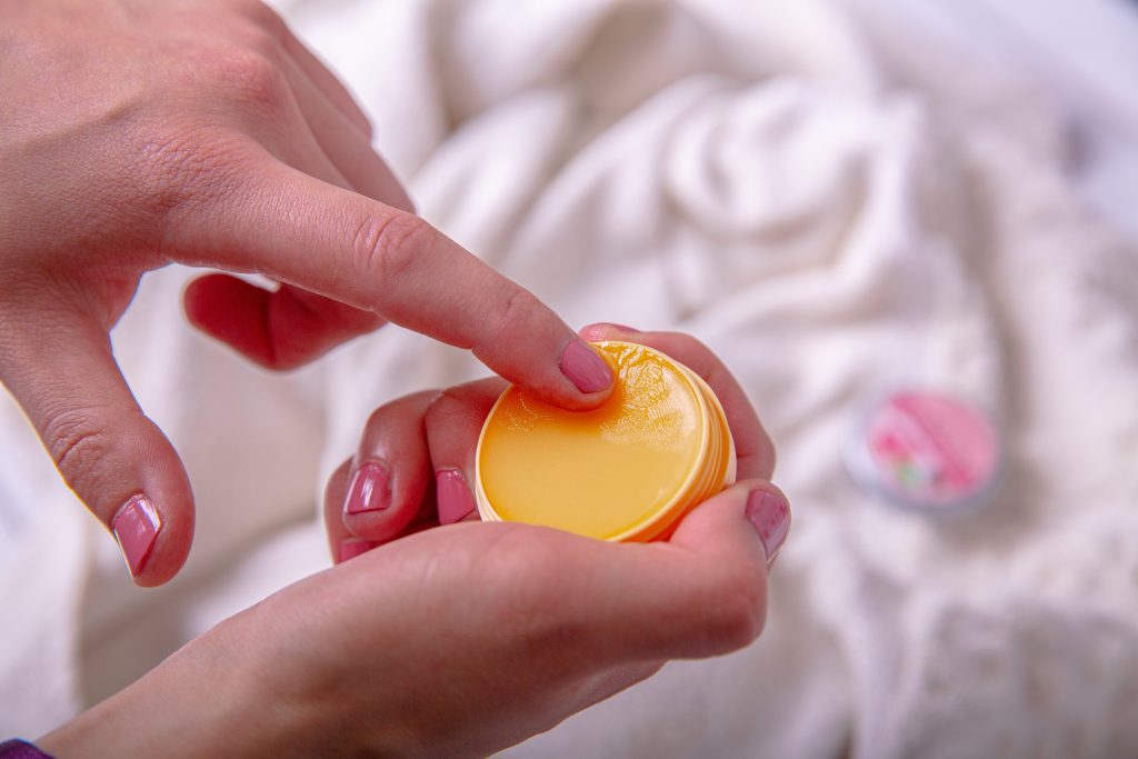 A hand getting a bit of homemade lip balm from a container
