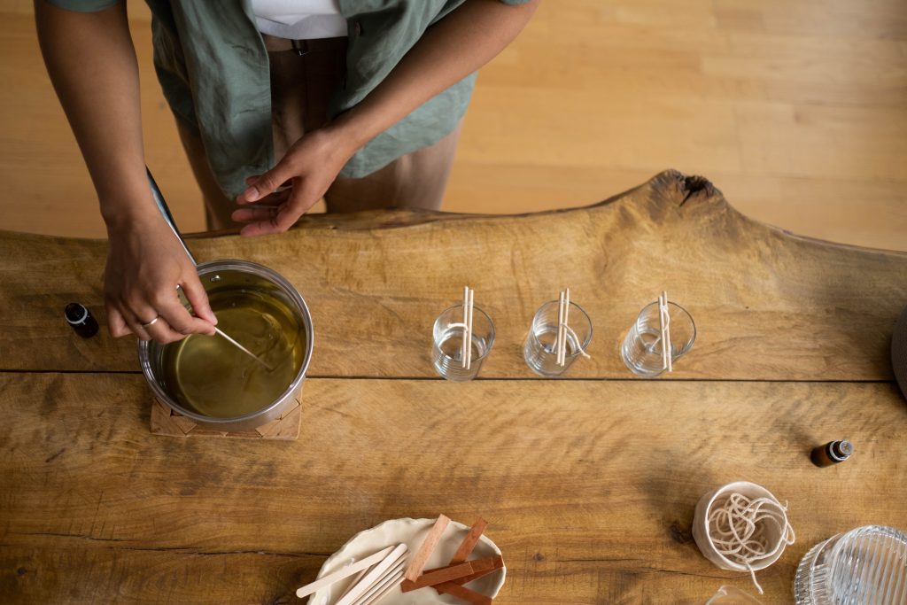 A person is mixing melted paraffin wax and fragrance oils to pour the mixture into the prepared glasses with wicks