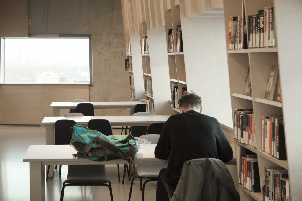 A physiotherapist at a library, sitting at a table with their jacket behind them