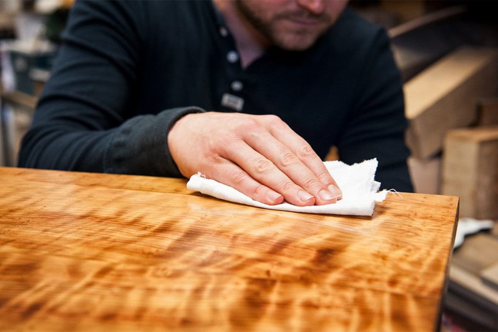 A person is rubbing paraffin wax on a wooden wooden table