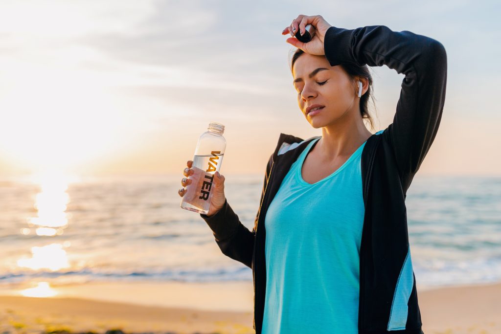 A lady looks dehydrated while holding her water bottle on a clean beach