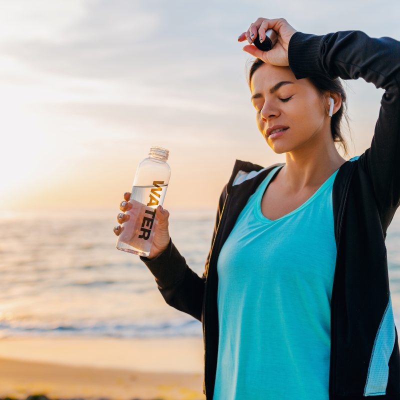 A lady looks dehydrated while holding her water bottle on a clean beach