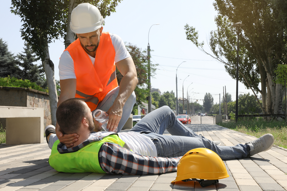 A person is helping another person through their heat stroke while wearing their hard hats and vests
