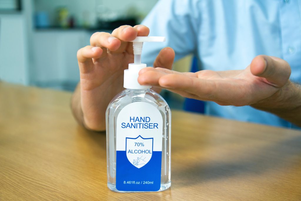 A person is putting on hand sanitizer with 70% alcohol in it on their hands while the bottle is on a wooden table