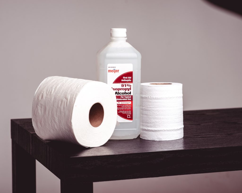 a bottle of isopropyl alcohol is nestled in between two rolls of toilet paper while on top of a wooden table