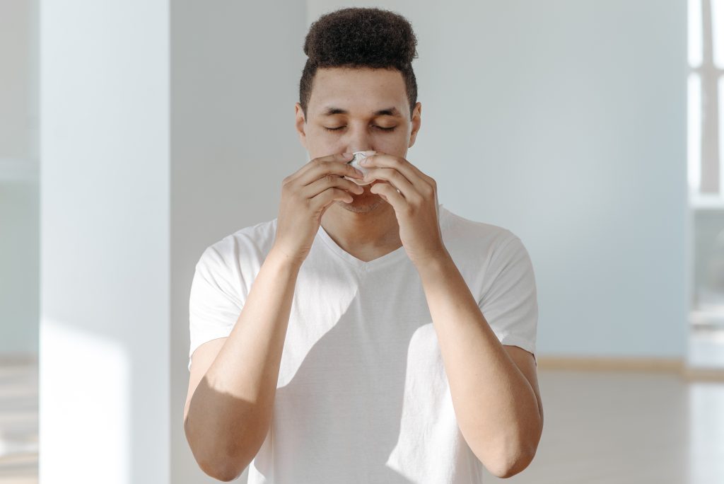 A person who has allergies is sneezing into a tissue in both of his hands