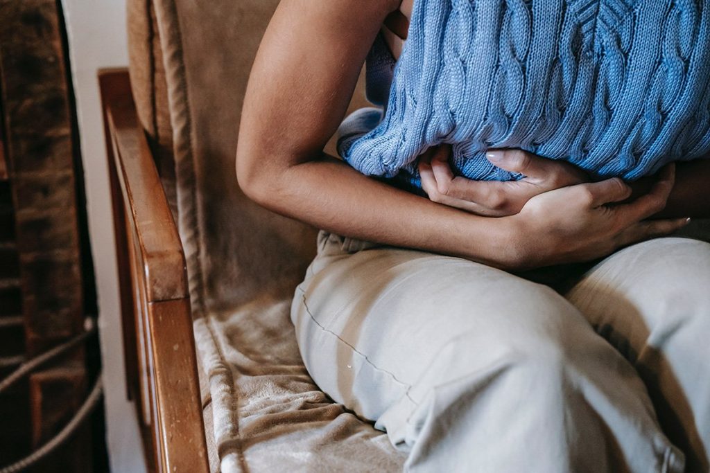 A woman is having digestive difficulties while sitting down on a chair