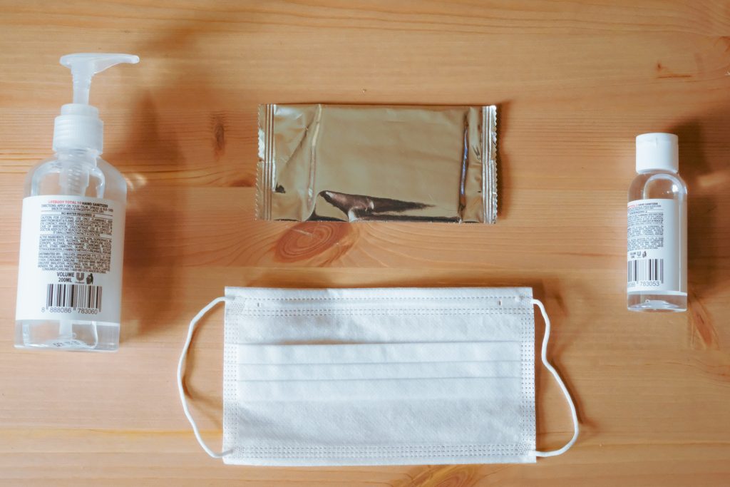 alcohol-based sanitizers and wipes with a face mask are on a wooden table