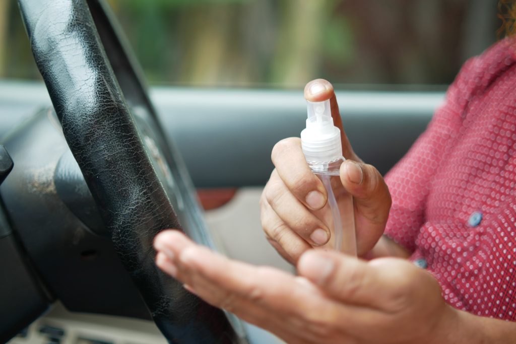 a person is spraying ethyl or isopropyl alcohol on their hands while sitting behind the wheel of their car
