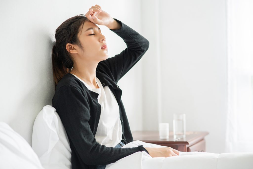 A person is sitting up on their bed, on the verge of a possible fainting spell