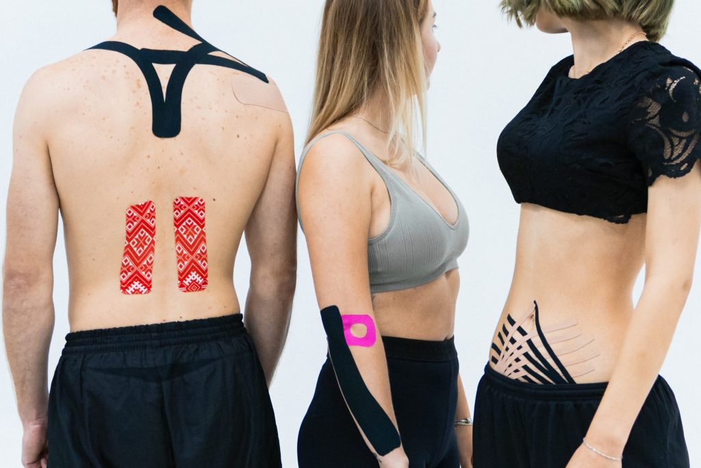 Three people are showing the different places on their body where they put the kinesio tape on, like the shoulder or the stomach