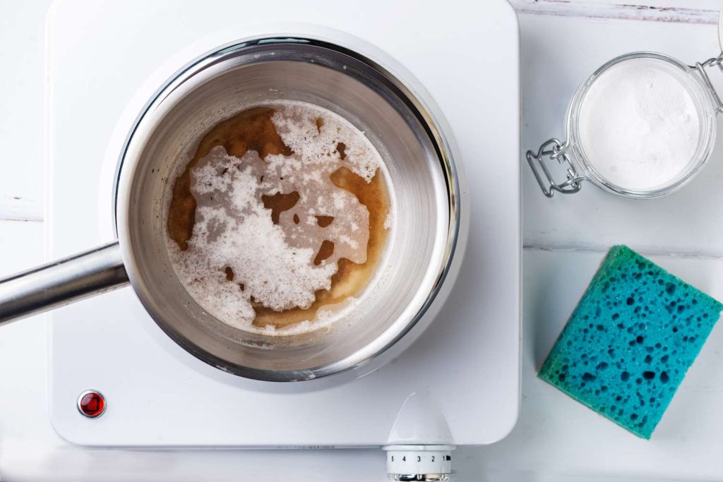 A pot of Epsom salt and water is on a stove while a sponge and a canister of Epsom salt is at the side