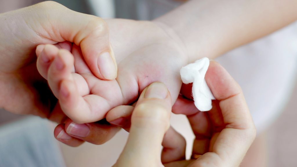 A person is trying to remove a splinter in a child's hand, holding it while rubbing a cotton ball on it