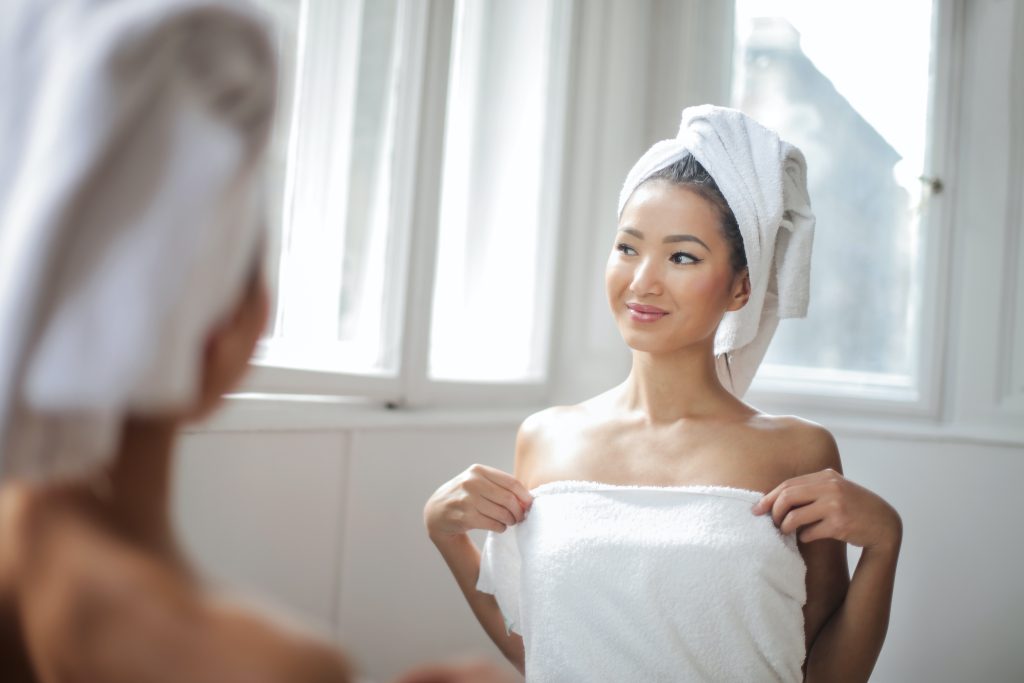 A woman after an Epsom salt bath, wearing two towels and standing in front of a mirror