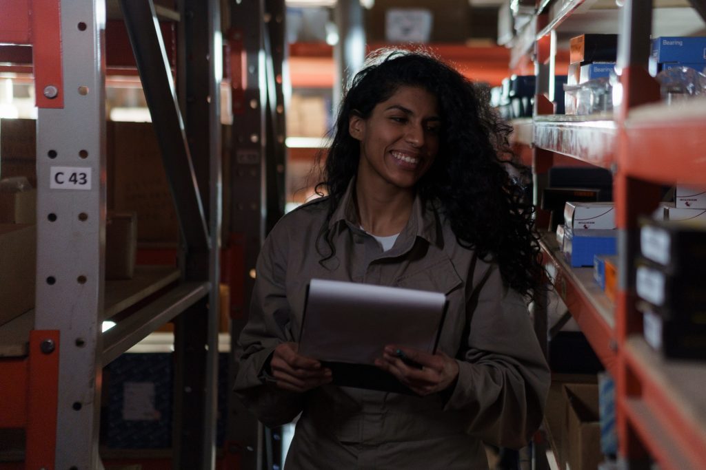 An employee of a supplier of physiotherapy products  looking through their own inventory with a list in her hands and a smile on her face