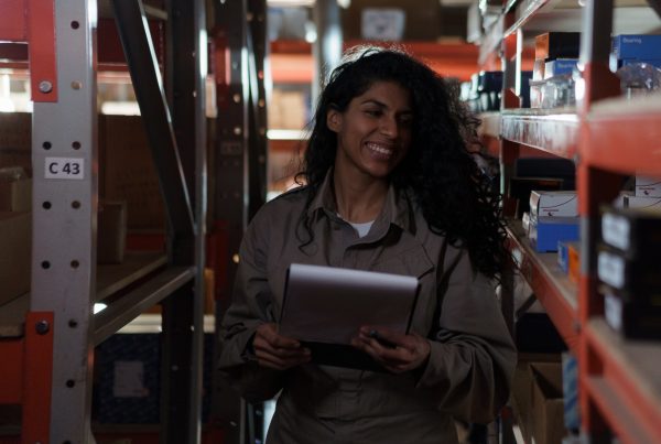 An employee of a supplier of physiotherapy products looking through their own inventory with a list in her hands and a smile on her face