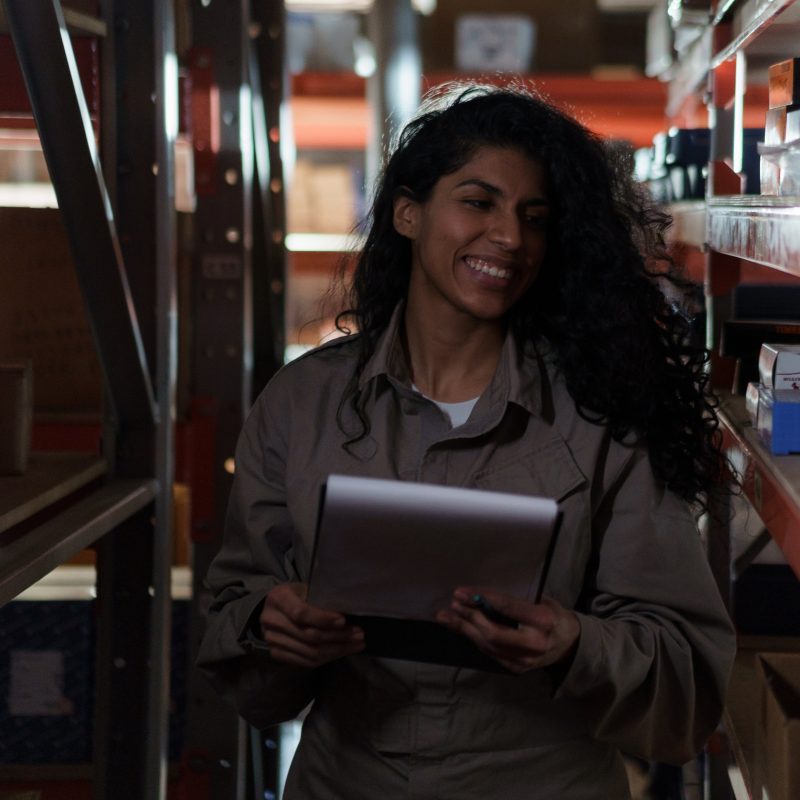 An employee of a supplier of physiotherapy products looking through their own inventory with a list in her hands and a smile on her face