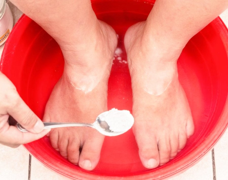 A person is putting in some Epsom salt in the basin of water where their feet are already submerged in