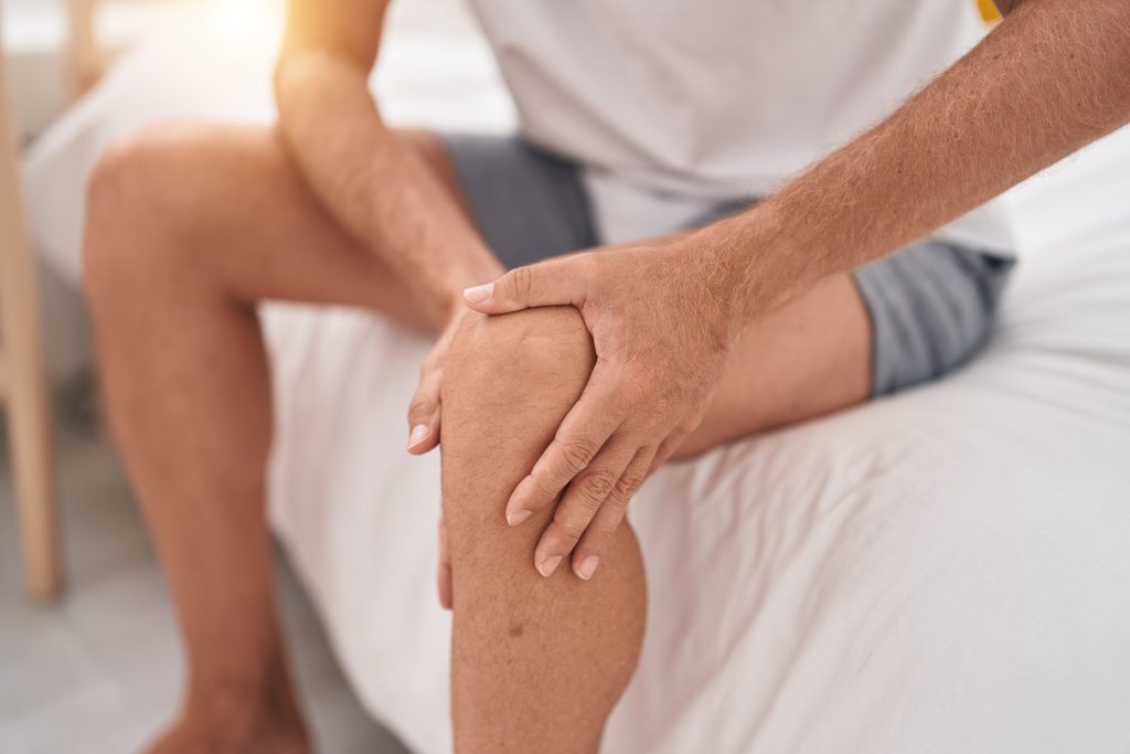 A person is sitting on the side of their bed while holding onto their aching joints