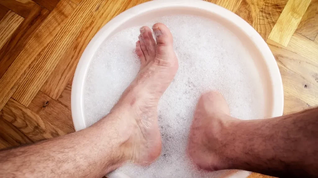 A person is having an Epsom salt foot soak, putting their feet in a basin on the wooden floor