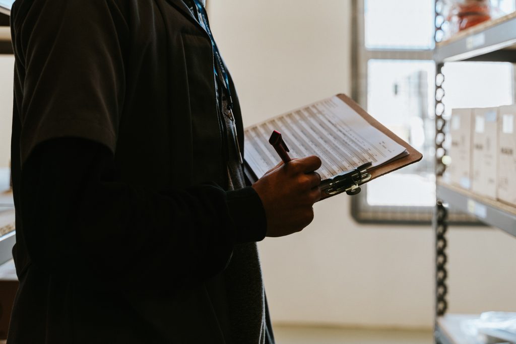 A physiotherapy clinic employee checking their limited inventory while holding a clipboard with their list and a pen in their hands