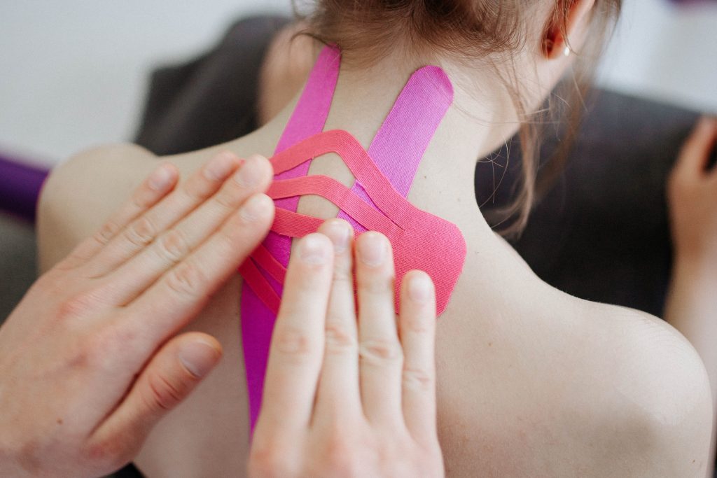 A person is putting on two sets of oink KT tape on the back of the neck of another person