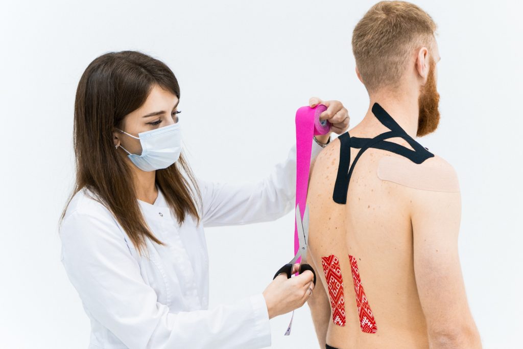 A physiotherapist is putting KT tape, cutting it before placing the tape on the back of their patient