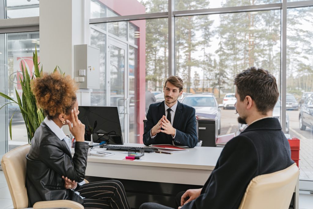 a physiotherapy clinic employee is talking to two of their clients while behind a desk