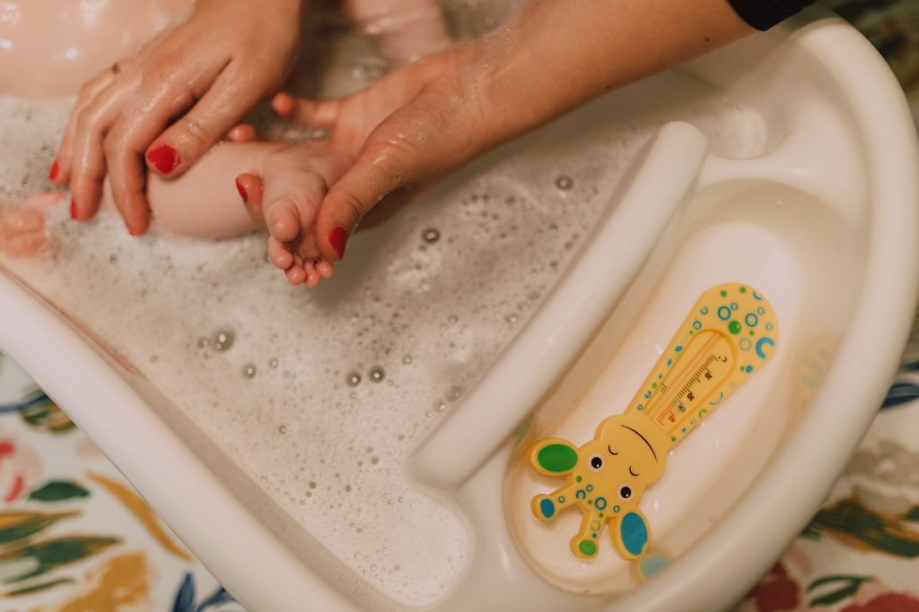 A person is bathing a baby with an Epsom salt bath in a baby bathtub, rubbing the baby's feet clean