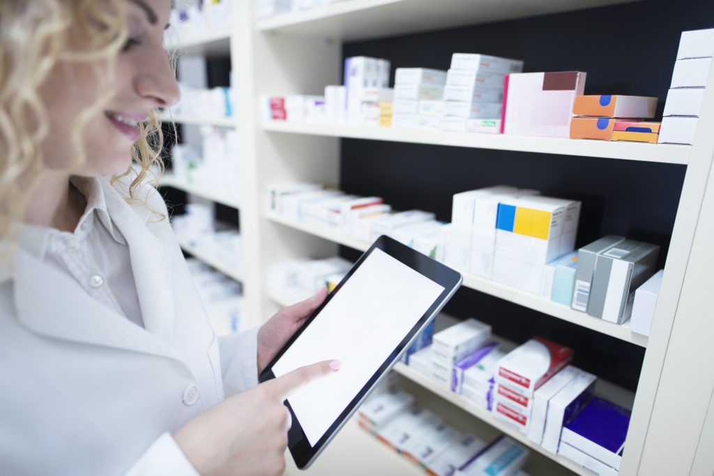 A physiotherapy clinic employee is looking through the clinic's inventory with a tablet in their hands and wearing a white coat